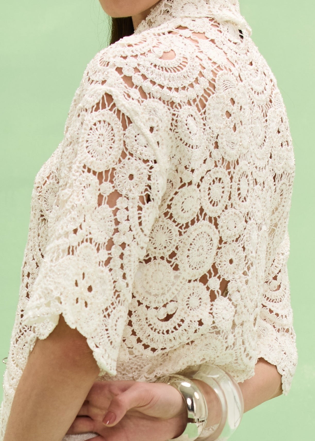 Close-up of a person wearing a white lace top against a light green background
