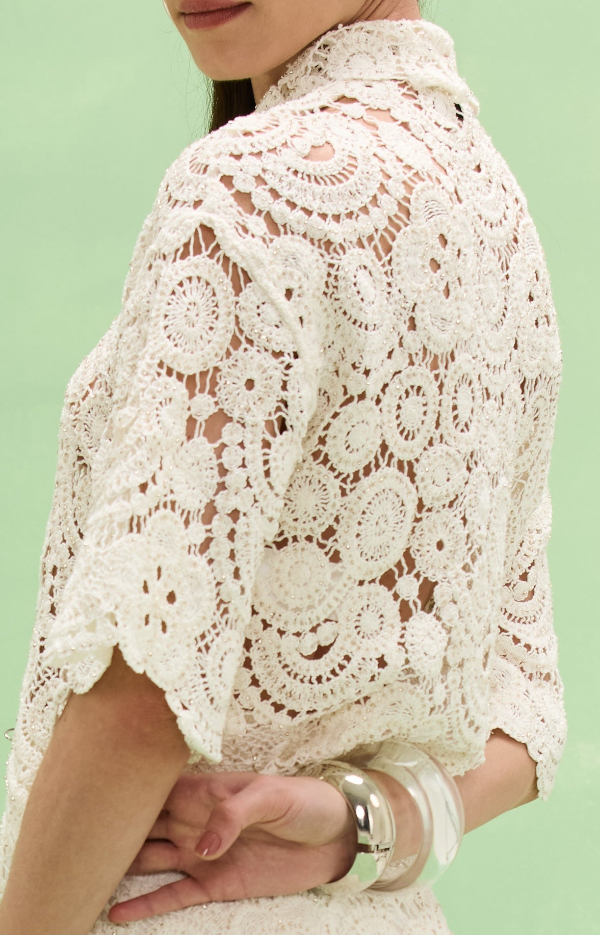 Close-up of a person wearing a white lace top against a light green background