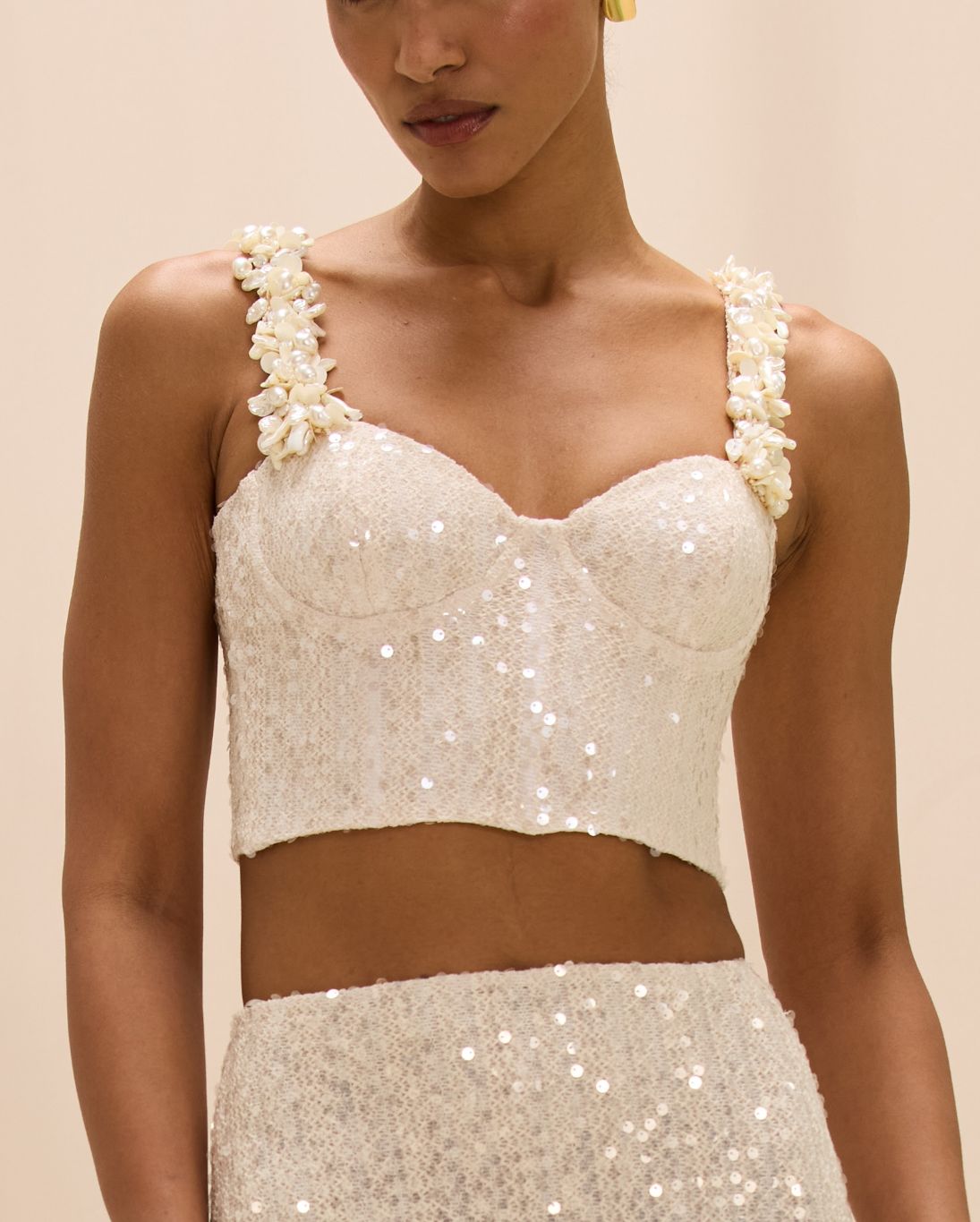 White sequin top with floral straps worn by a model on a beige background