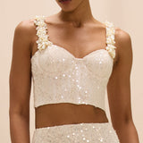 White sequin top with floral straps worn by a model on a beige background