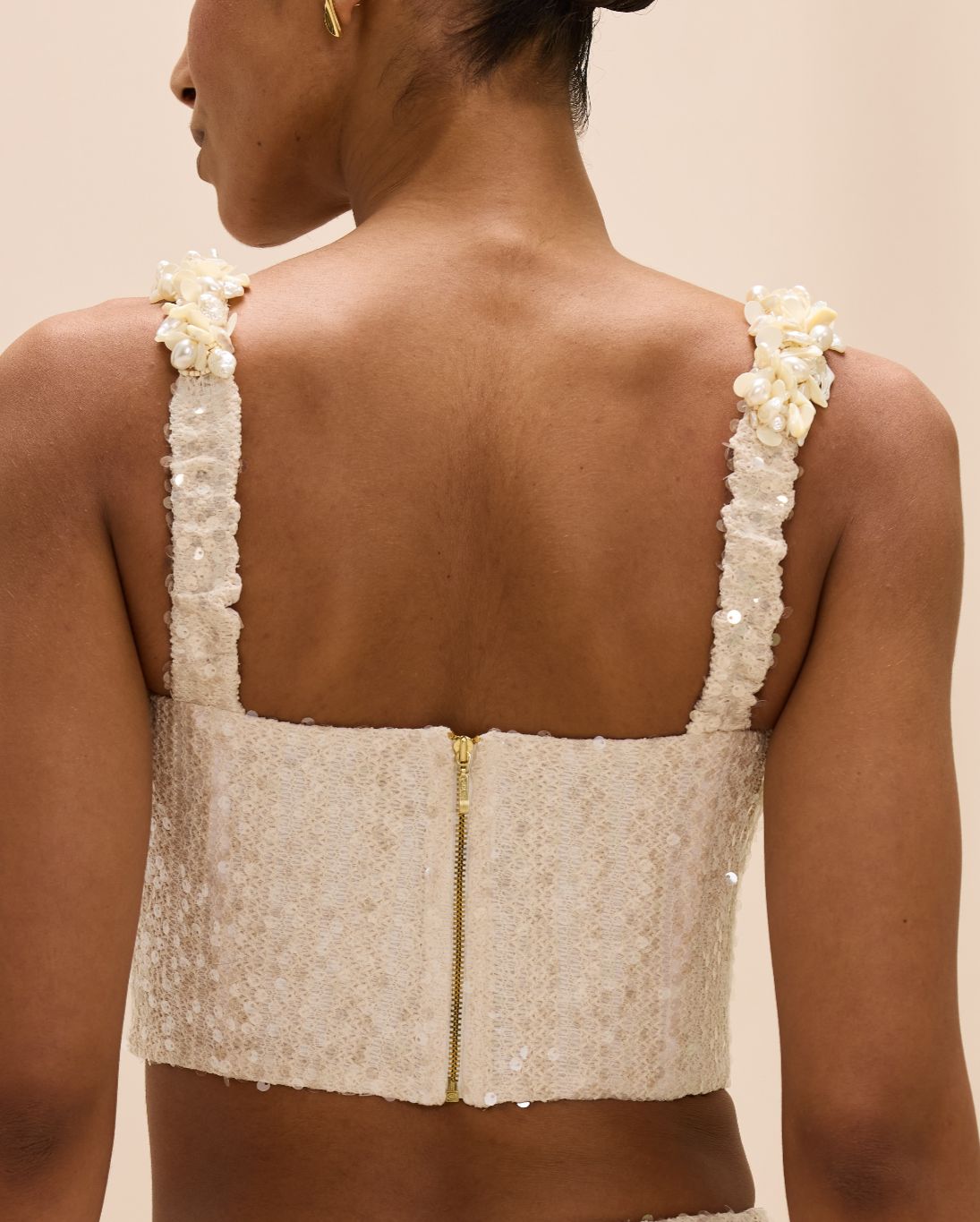 Beige lace top with pearl straps worn by a person on a beige background