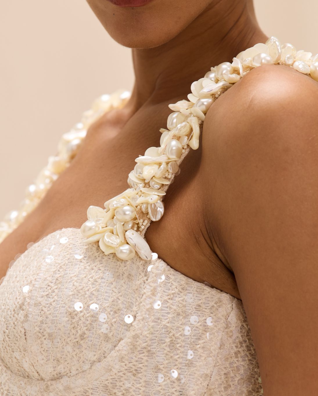 Close-up of a person wearing a pearl and sequin dress with a neutral background