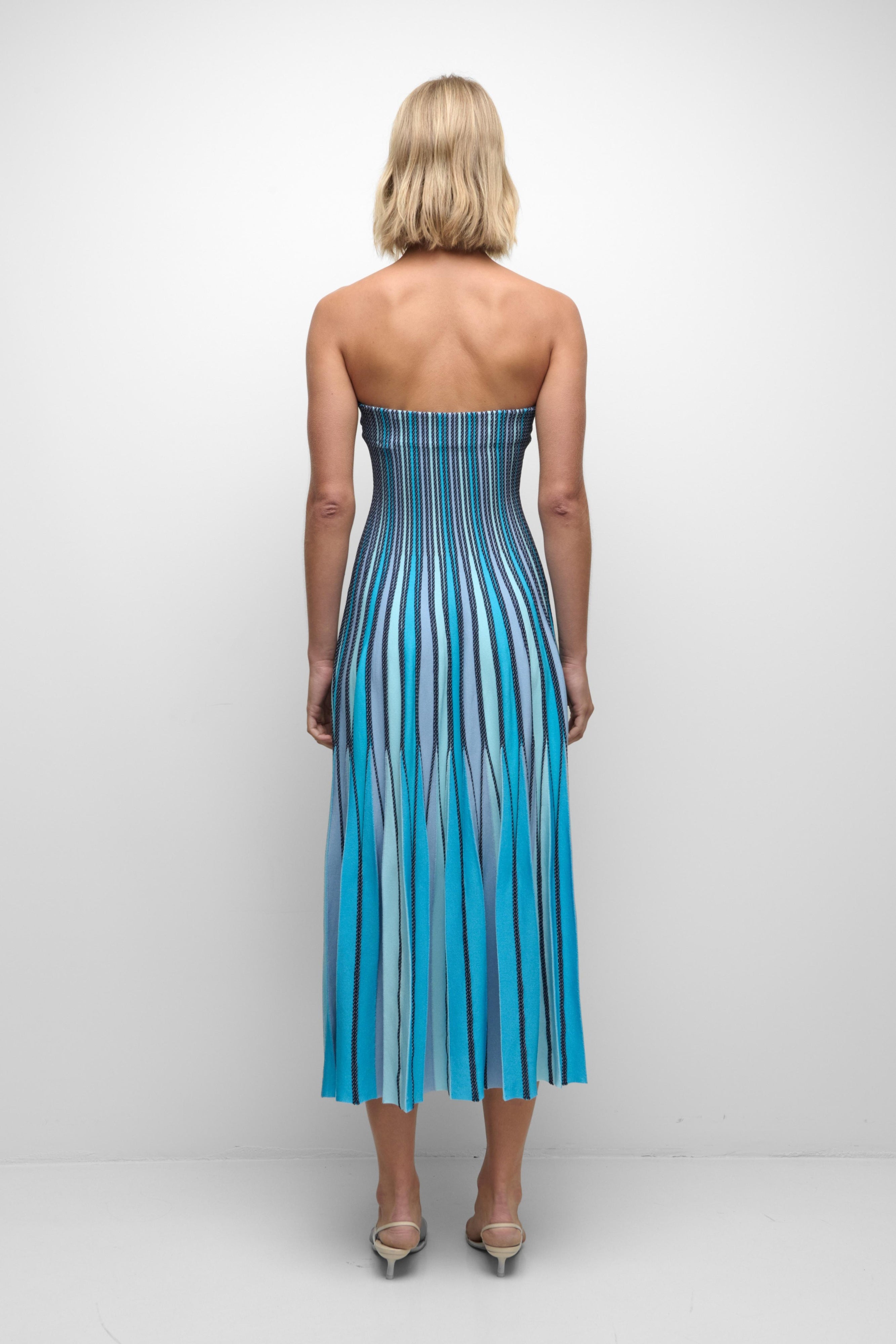 Woman wearing a strapless blue and white striped dress on a plain background