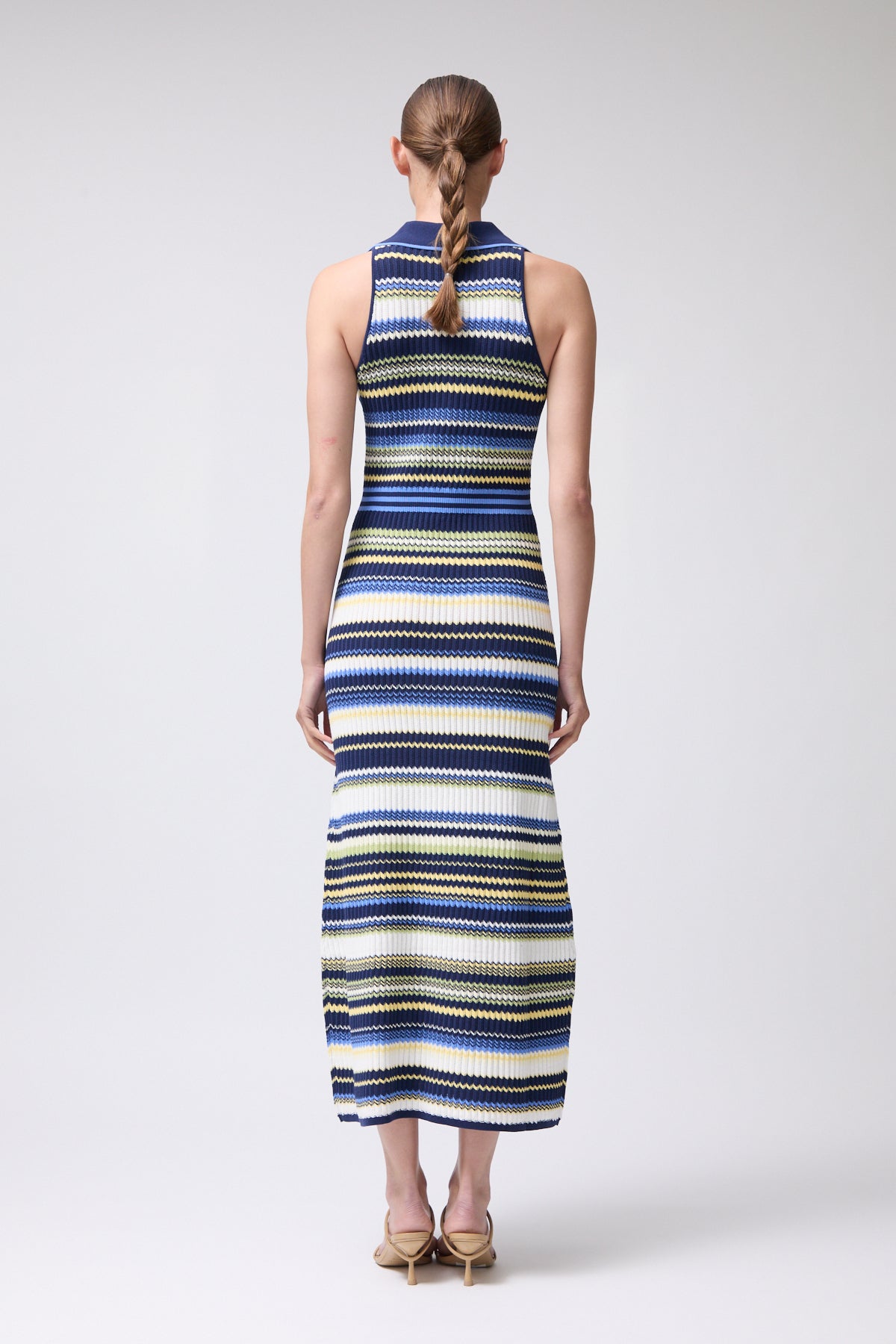 Woman wearing a long, sleeveless dress with blue and yellow stripes on a white background
