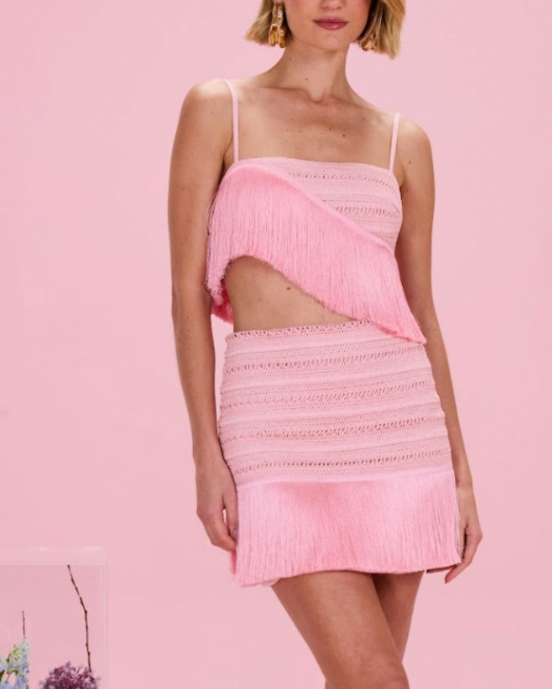 Woman wearing a pink crochet top and skirt set against a pink background