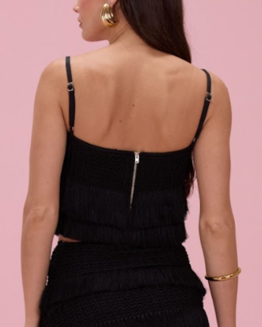 Person wearing a black top with thin straps against a pink background