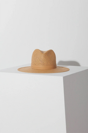 A sand-colored Janessa Leoné Simone hat with a packable straw brim and a monochromatic leather band, displayed on a white pedestal.